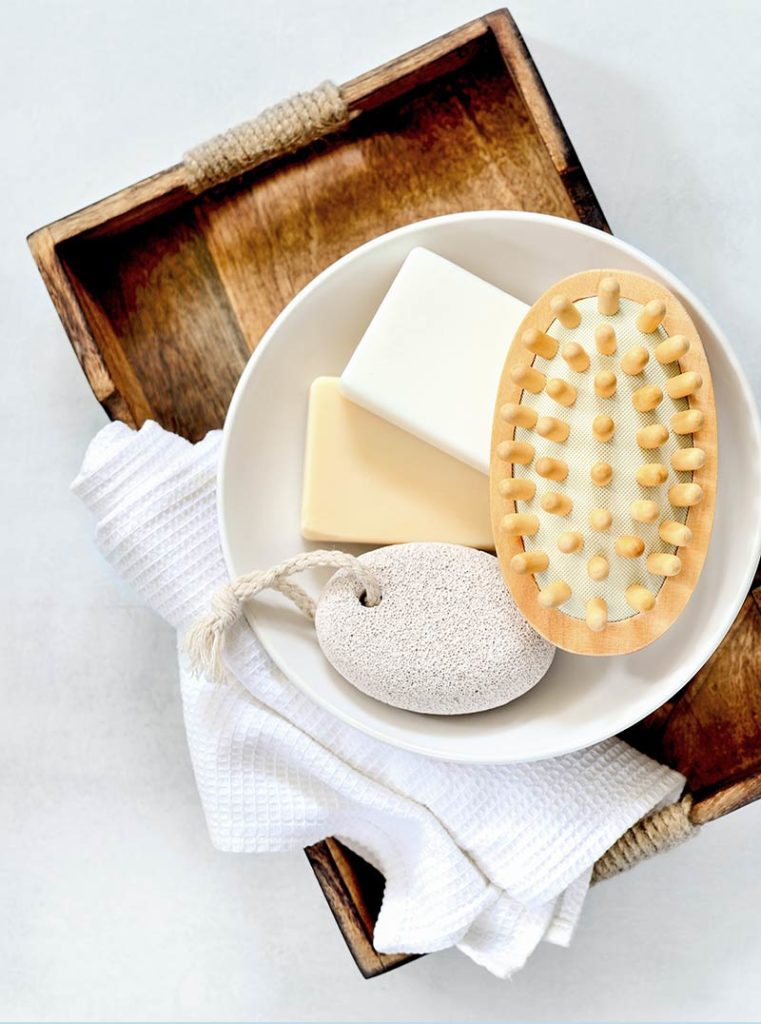 A bowl of soap and a bath brush on a wooden tray.